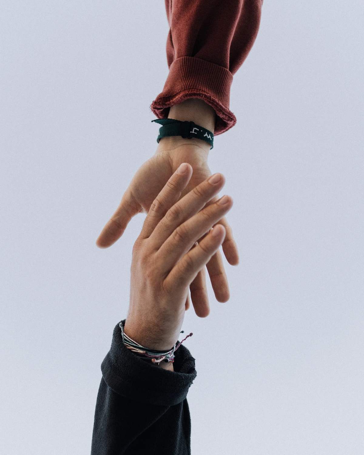 One hand reaching out to take another against a pale sky