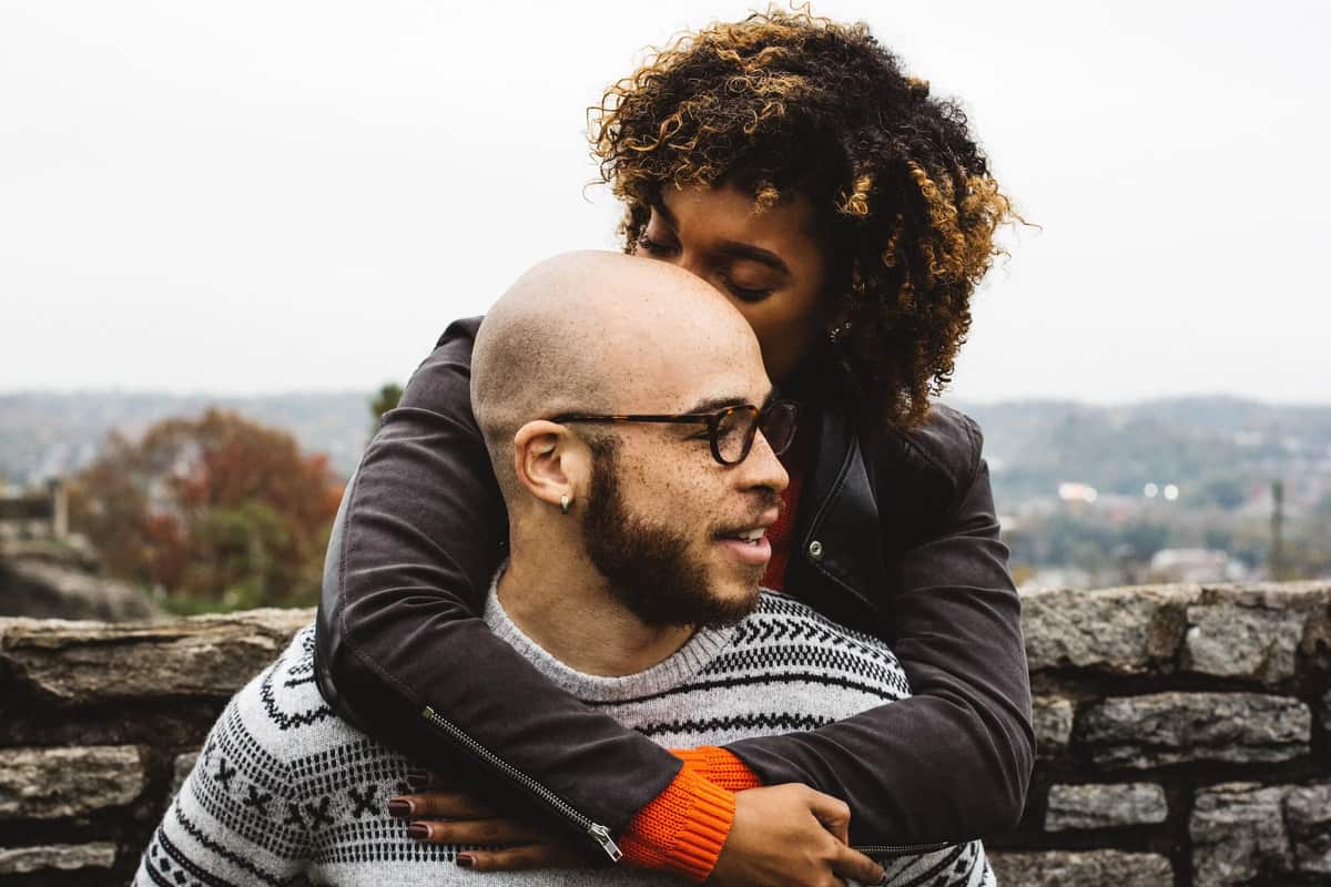 A woman hugging her smiling husband from behind on a stone overlook